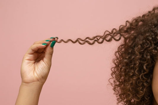 Close-up de uma mulher latina com unhas pintadas de verde segurando um cacho de cabelo depois de sua transição capilar. 