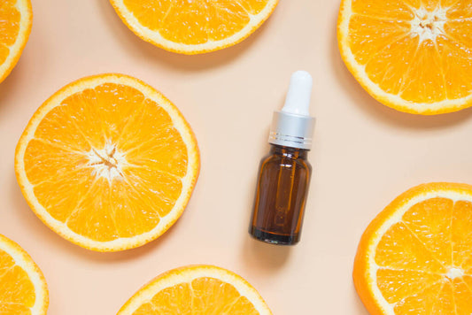 Frasco de conta-gotas com sérum de vitamina C para a pele, cercado por fatias frescas de laranja sobre um fundo claro